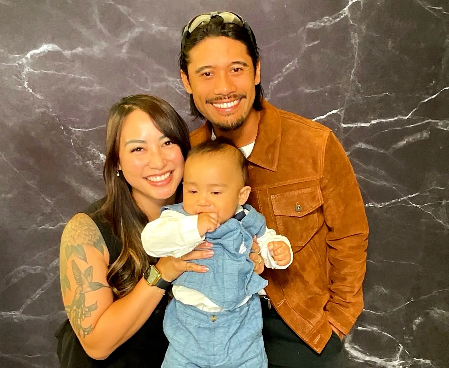 Parents posing with their baby against the black marble photo booth backdrop