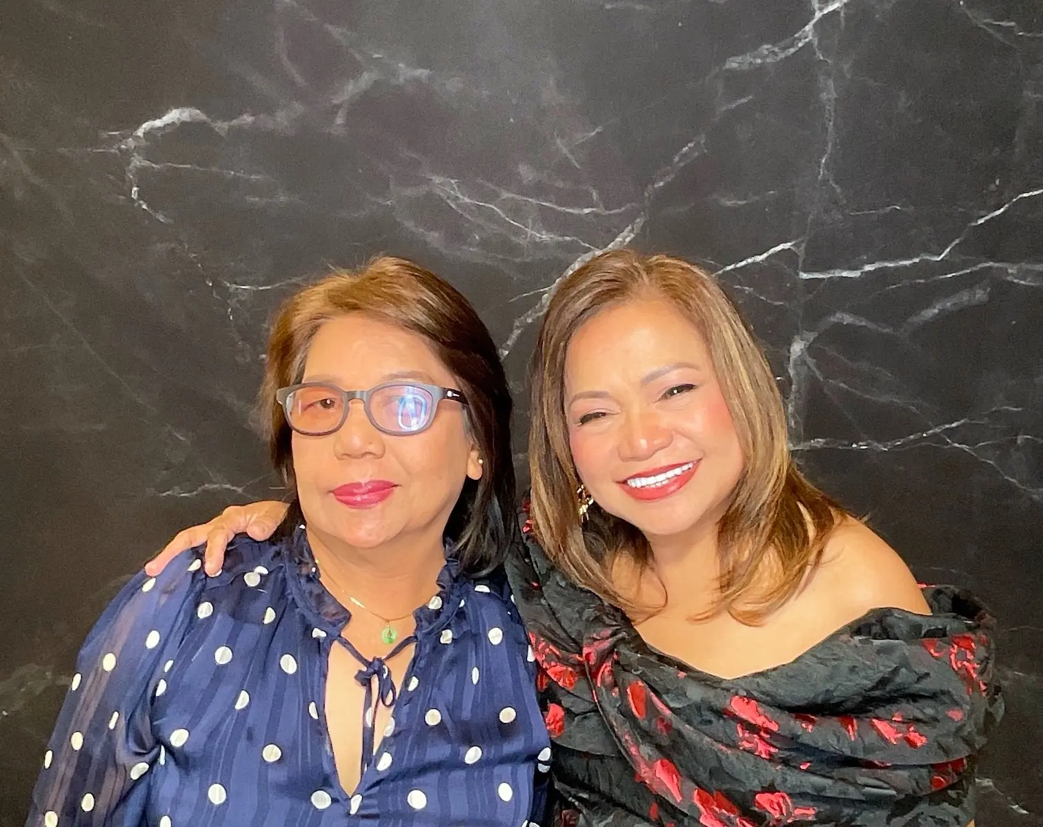 Two guests smiling together against the black marble photo booth backdrop