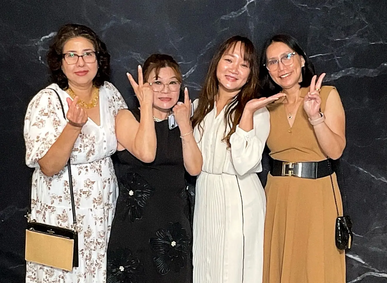 Four retirement party guests posing with finger hearts and peace signs