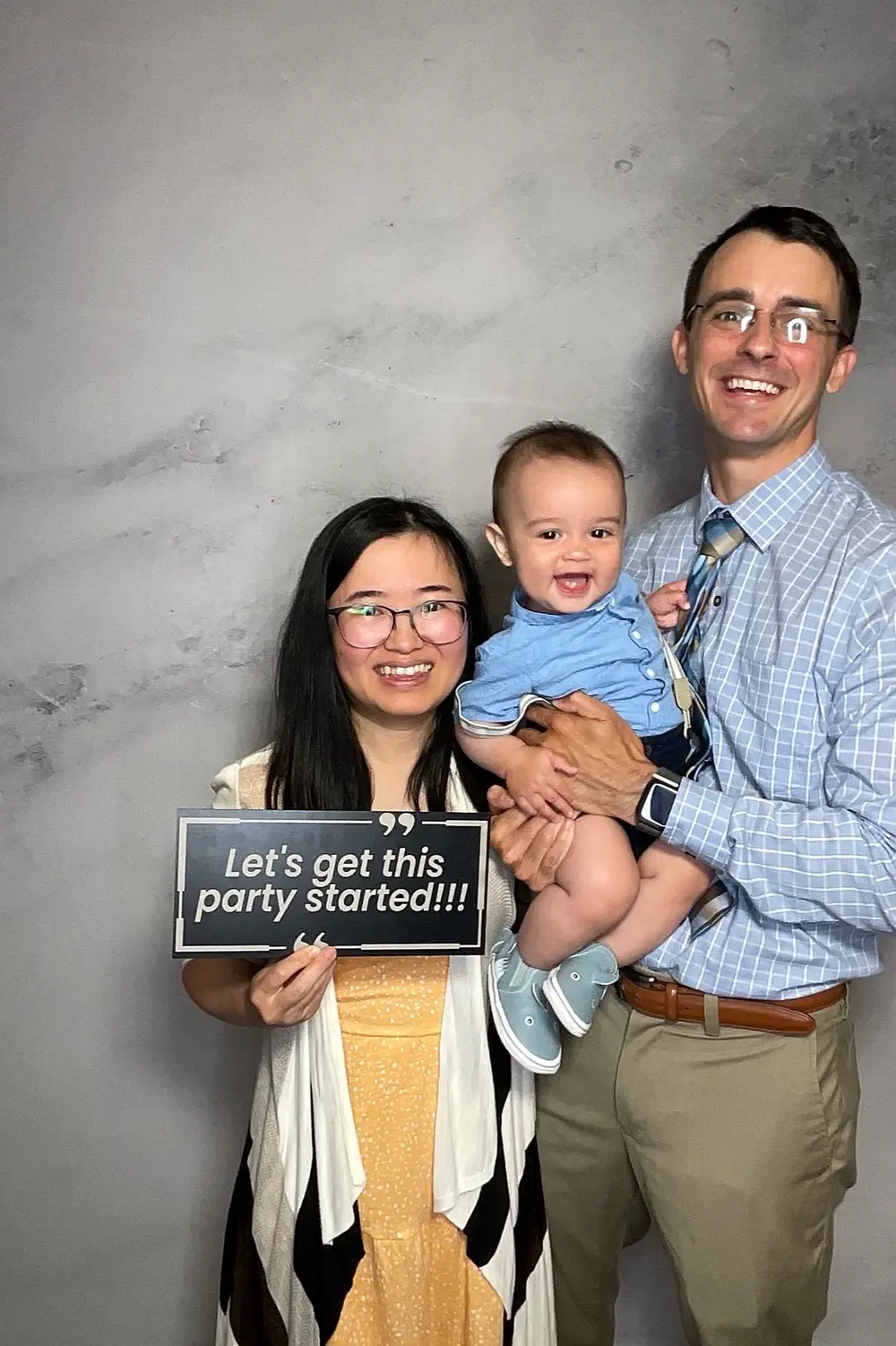 Wedding guests holding a baby and a party-started photo booth sign