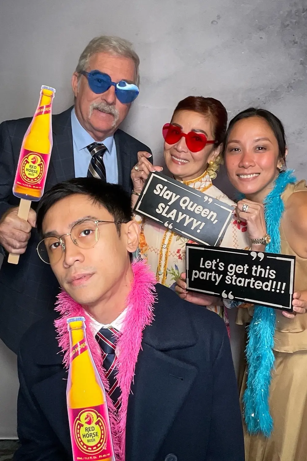 Four wedding guests wearing colorful glasses and posing with playful signs