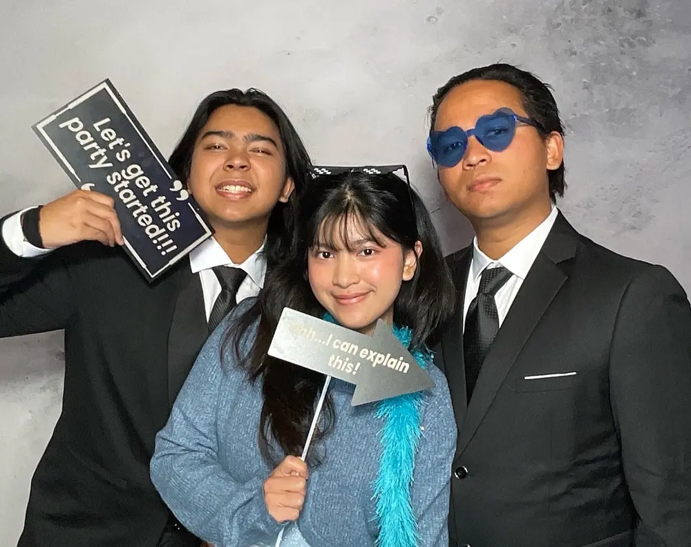Three wedding guests posing with signs and colorful photo booth props