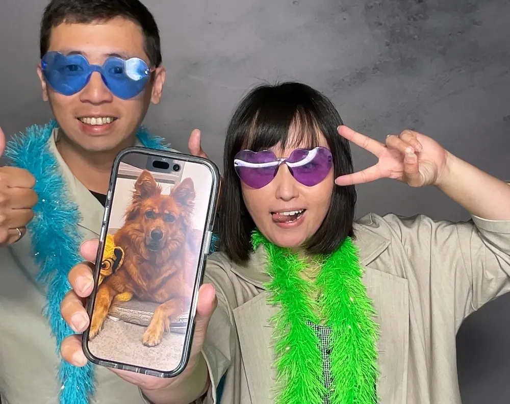 Two wedding guests posing with a phone and bright party accessories