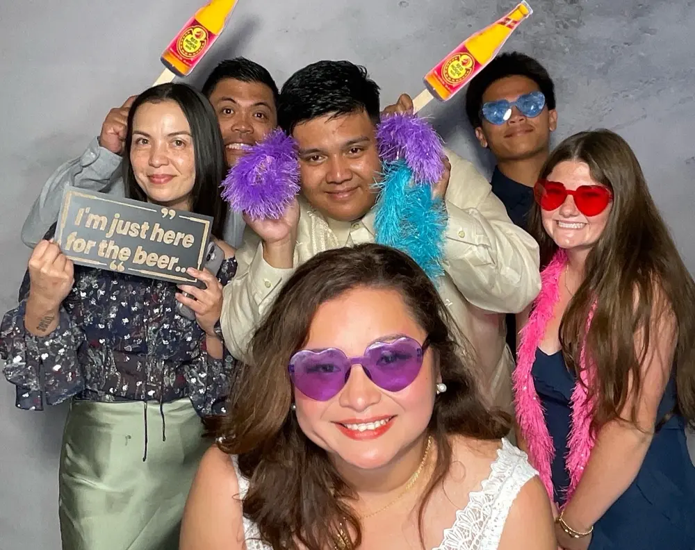 Bride surrounded by friends wearing colorful wedding photo booth props