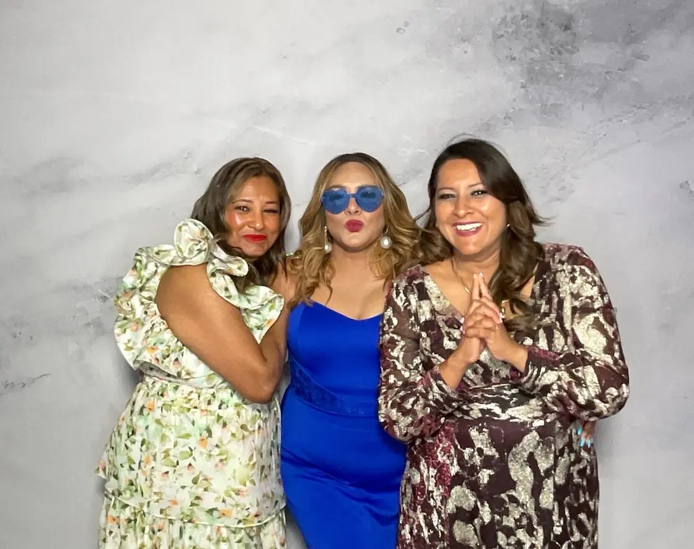 Three wedding guests posing together in front of a marble photo booth backdrop
